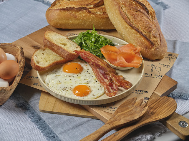 Full breakfast platter with sunny side eggs, crispy bacon, smoked salmon, arugula, and toasted sourdough at Prettiplatters